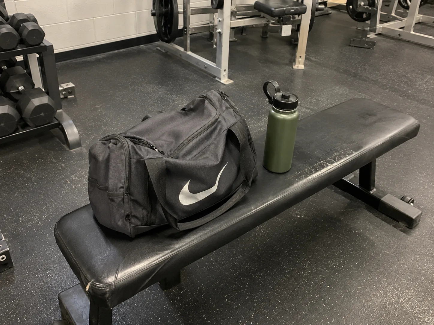 A gym bag and water bottle on a bench, photographed casually from a few steps away.
