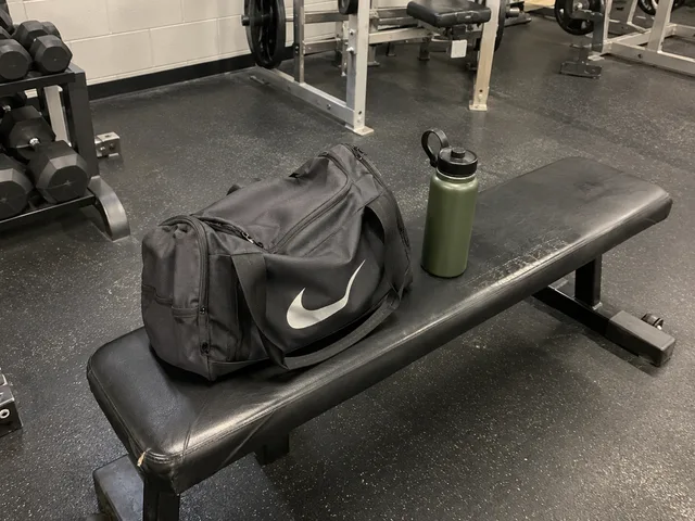 A gym bag and water bottle on a bench, photographed casually from a few steps away.