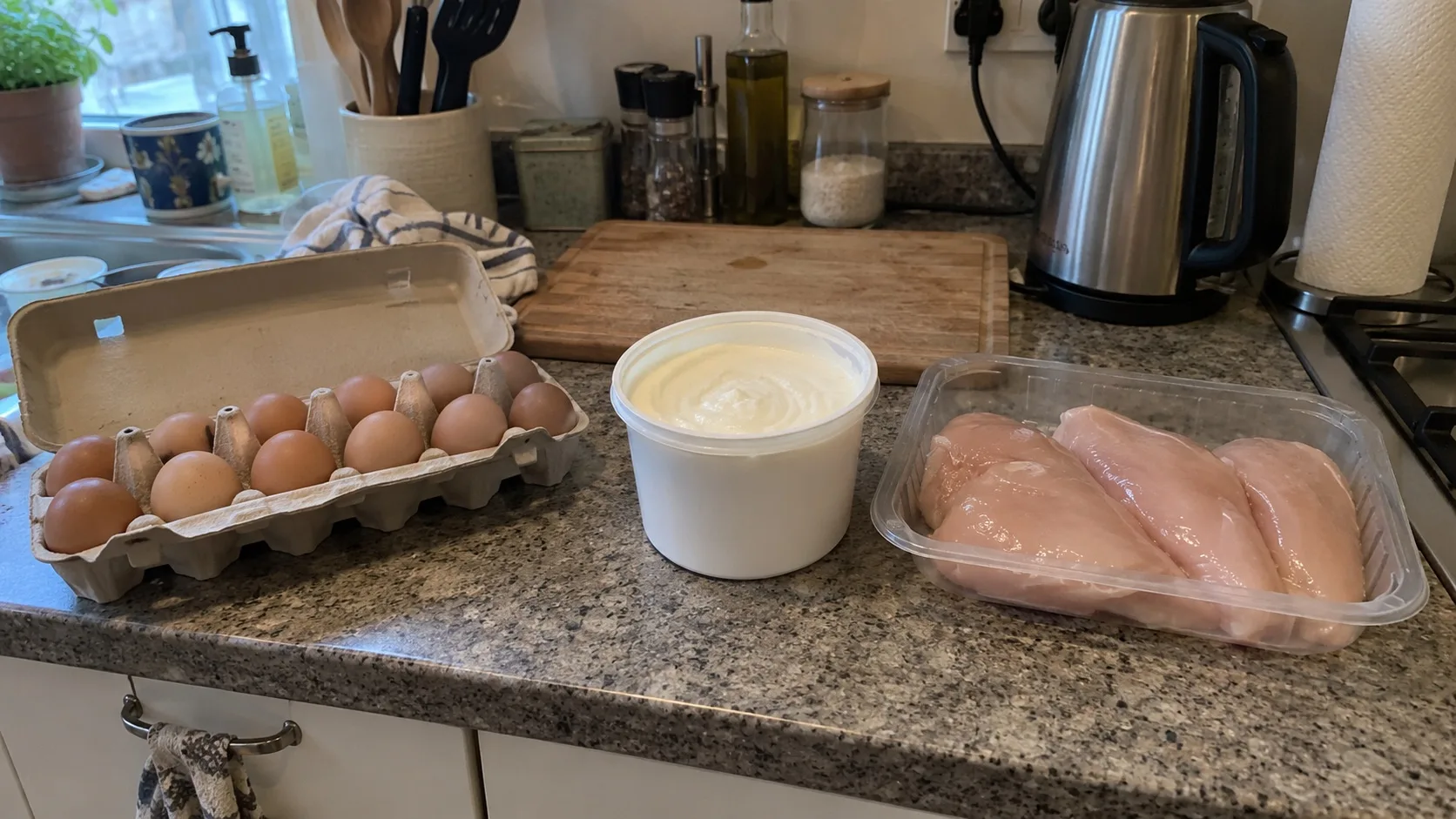A carton of eggs, a pot of plain Greek yogurt and a pack of raw chicken breast on an ordinary home kitchen counter.