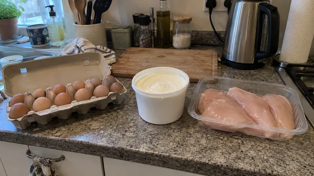 A carton of eggs, a pot of plain Greek yogurt and a pack of raw chicken breast on an ordinary home kitchen counter.
