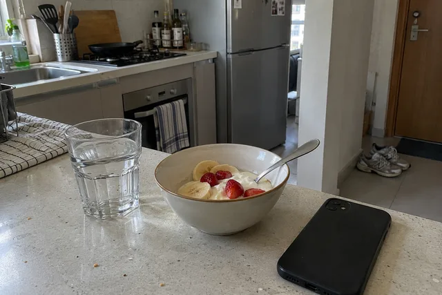 A glass of water, fruit yoghurt and a phone on a kitchen counter, with trainers near the door.
